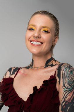 Modern bir stüdyoda kendine güvenen genç bir kadın sanatsal dövmelerini ve parlak sarı makyajını gösteriyor..