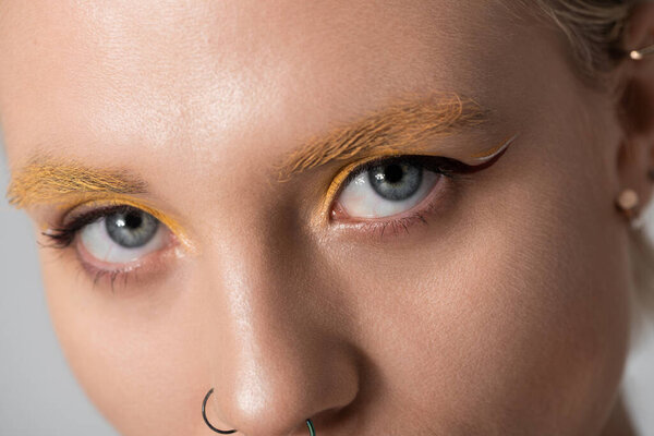 Captivating young woman with vibrant makeup stands against a soft background, exuding confidence.