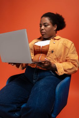Havalı bir sonbahar giysisi içinde şık bir Afro-Amerikan kadın stüdyoda dizüstü bilgisayar kullanıyor..