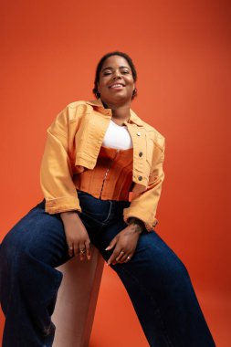 Kendine güvenen, iri yarı, Afro-Amerikan bir kadın şık bir sonbahar elbisesi içinde poz veriyor..