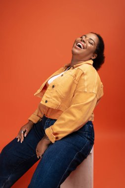 Neşeli, iri yapılı Afrikalı Amerikalı bir kadın, modaya uygun sonbahar kıyafetini stüdyoda sergiliyor..