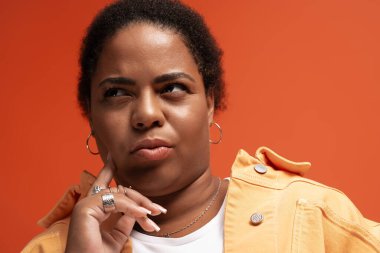 Düşünceli, iri yarı siyahi bir kadın canlı bir stüdyoda şık bir sonbahar kıyafetinin modelliğini yapıyor..