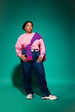 Stüdyoda modaya uygun bir sonbahar giysisi modelleyen şık, iri yarı siyahi bir kadın..