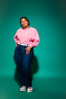 Kendine güvenen ve cüsseli bir kadın renkli bir stüdyoda modaya uygun bir sonbahar kıyafeti modelliyor..