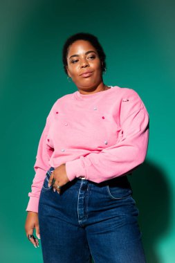 Kendine güvenen ve cüsseli bir kadın şık bir sonbahar kıyafetini canlı bir stüdyo arkaplanında modelliyor..