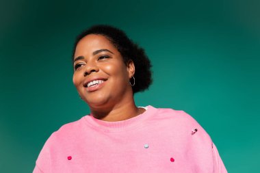 Kendine güvenen, iri yarı, Afro-Amerikan bir kadın parlak bir stüdyoda şık bir sonbahar kıyafeti modelliyor..