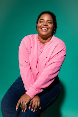 Kendinden emin ve cüsseli bir kadın modaya uygun sonbahar kıyafetini sergiliyor ve stüdyoda neşe saçıyor..