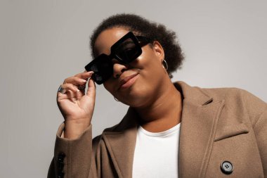 Parlak bir stüdyoda, iri yarı siyahi bir kadın şık sonbahar kıyafetini gösterir..