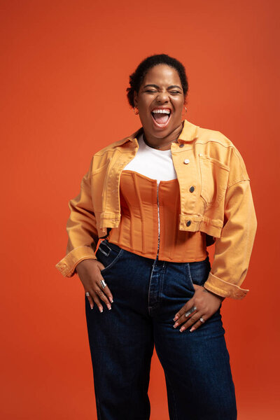 Уверенная в себе афроамериканка plus size моделирует триумфальный осенний наряд в яркой студии.