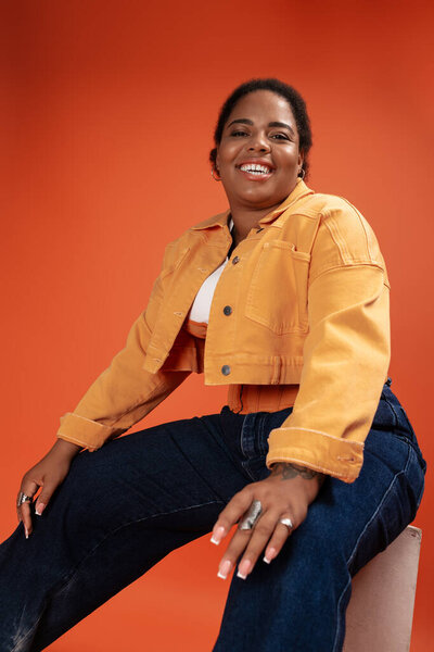 Уверенная в себе африканская женщина plus size позирует в триумфальном осеннем наряде, стилистическом стиле.