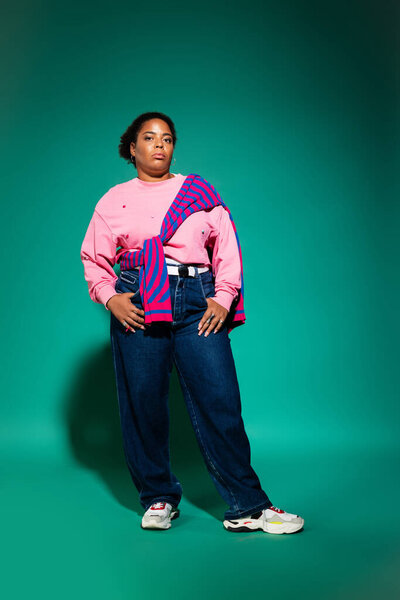 Стильная чернокожая женщина plus-size моделирует триумфальный осенний наряд в ателье.