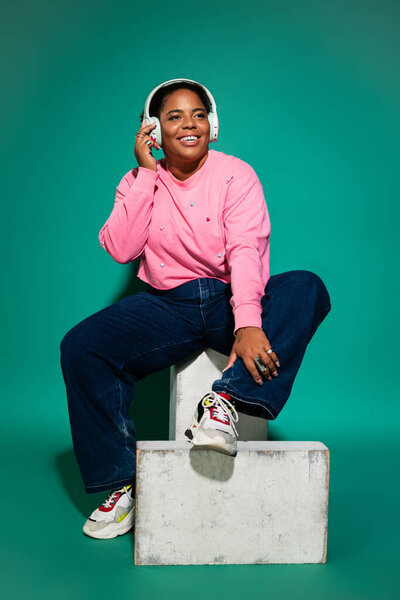 A plus-size Black woman smiles in a trendy autumn outfit, enjoying music.