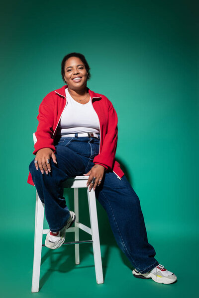 A confident plus-size African American woman smiles in a stylish autumn outfit in a studio.