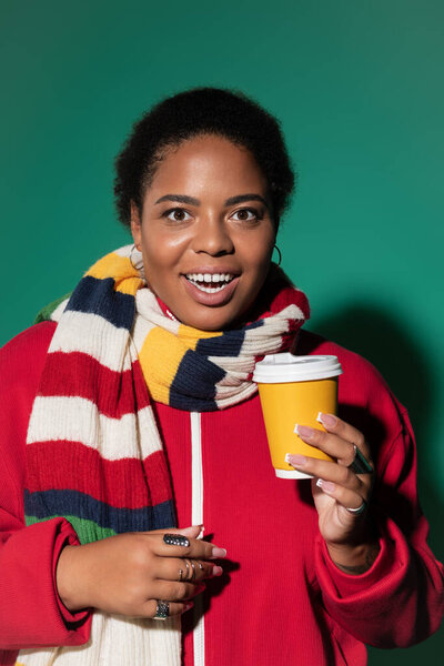 A stylish plus-size Black woman sips coffee while wearing an autumn-colored scarf.