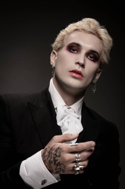 Yakışıklı adam şık bir Cadılar Bayramı kostümü içinde, koyu renk makyaj ve benzersiz giysiler giyiyor..