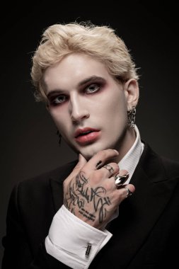 Efsanevi Cadılar Bayramı kostümü giymiş genç bir adam dramatik makyaj ve aksesuar giyerek kendinden emin poz verir..