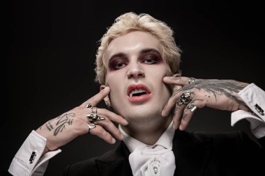 Genç bir adam dramatik makyaj ve şık mücevherlerle süslenmiş destansı Cadılar Bayramı kostümünü sergiliyor..