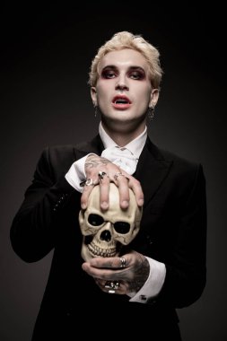 Genç bir adam çarpıcı Cadılar Bayramı kostümünü sergiliyor, kendine güvenen bir kafatası tutuyor..