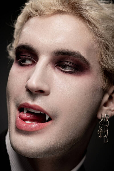 A young handsome man in a striking Halloween costume displays bold makeup and fangs.