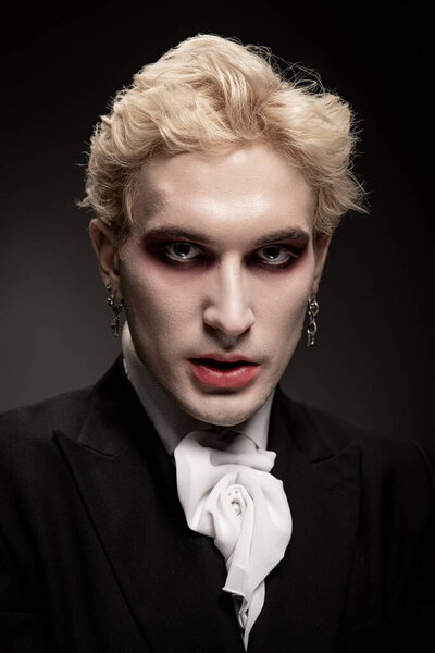 A young man confidently poses in a bold Halloween costume with striking makeup and attire.
