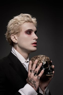 Yakışıklı genç adam destansı bir cadılar bayramı kılığına bürünmüş, elinde dekoratif bir kafatası tutuyor..