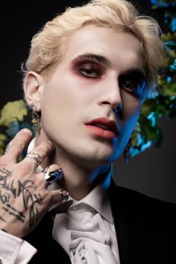 Genç bir adam bir partide çarpıcı Cadılar Bayramı kostümünü dramatik bir makyajla gösteriyor..