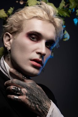 Genç ve yakışıklı bir adam dramatik makyaj ve kalın aksesuarlarla destansı Cadılar Bayramı kostümünü sergiliyor..