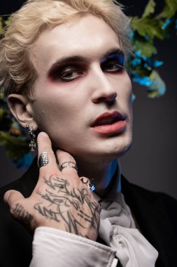 Genç adam etkileyici bir Cadılar Bayramı kostümü giyiyor. Makyaj ve kalın aksesuarları var..