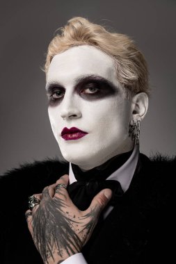 Genç bir adam çarpıcı bir Cadılar Bayramı kostümü sergiliyor dramatik makyajı ve şık bir kıyafeti var..