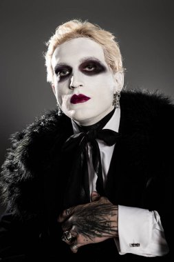 Çarpıcı bir Cadılar Bayramı kostümü içindeki genç adam dramatik makyajlı ve zarif pozlar veriyor..