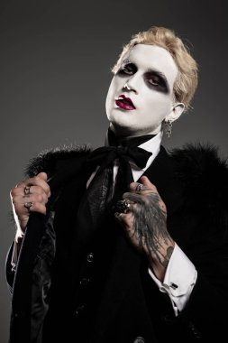 Göz alıcı genç bir adam, özenle hazırlanmış, koyu renk bir Cadılar Bayramı kostümü giymiş..