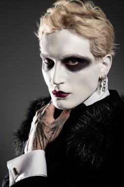 Şık bir genç adam, çarpıcı makyaj ve aksesuarlarıyla cesur bir Cadılar Bayramı kostümü sergiliyor..