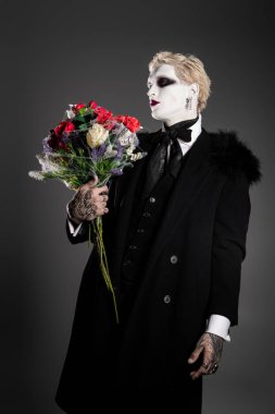 Genç ve yakışıklı bir adam süslü bir Cadılar Bayramı kostümü içinde elinde renkli bir buketle gururla duruyor..