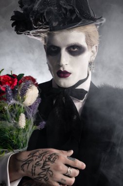 Karmaşık bir Cadılar Bayramı kostümü içindeki yakışıklı genç adam sisle çevrili canlı çiçekler tutuyor..