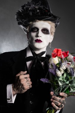 Karmaşık bir Cadılar Bayramı kostümü içinde büyüleyici bir genç adam canlı çiçekler tutar..