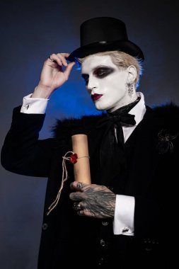 Müsrif bir Cadılar Bayramı kostümü giymiş genç adam elinde bir parşömenle dramatik bir poz veriyor.