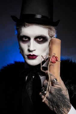 Destansı Cadılar Bayramı kostümü içinde çarpıcı bir genç adam elinde bir parşömen tutuyor ve yaratıcı görünümünü gösteriyor..