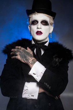 Genç bir adam eşsiz makyajı ve şık kıyafetleriyle muhteşem Cadılar Bayramı kostümünü gösteriyor..