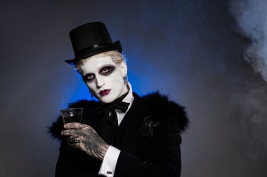 Genç yakışıklı bir adam dramatik makyajlı ve silindir şapkalı nefes kesici bir Cadılar Bayramı kostümü sergiliyor..