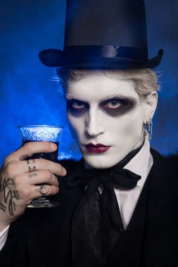 Yakışıklı genç adam elinde gizemli bir içki tutarken etkileyici bir Cadılar Bayramı kostümü giyiyor..