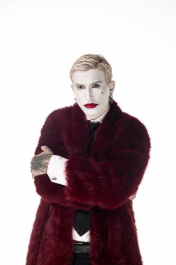 Joker kostümü giymiş genç bir adam gururla kırmızı kürk giyiyor..