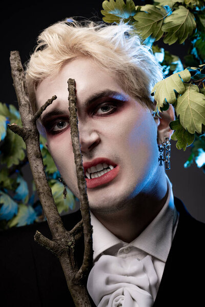 Handsome young man wears an extraordinary Halloween disguise, standing amidst eerie foliage.