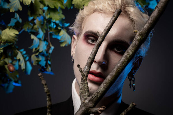 A young handsome man showcases his stunning Halloween costume among eerie foliage and branches.