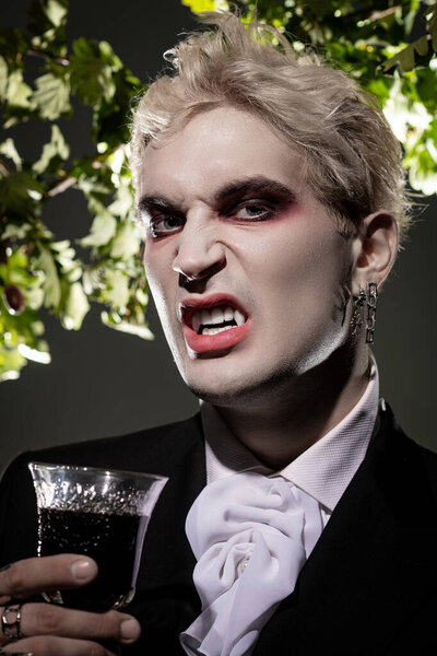 Молодой человек показывает творчество в эпичном костюме на Хэллоуин, смелый макияж и веселый напиток.