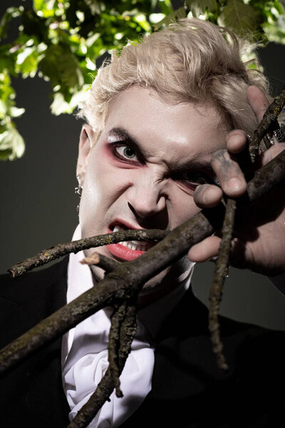 A young handsome man poses fiercely in an elaborate Halloween costume, holding branches as props.