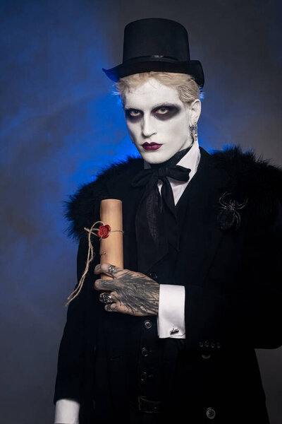 Молодой человек носит впечатляющий костюм на Хэллоуин с поразительным макияжем и таинственным свитком.