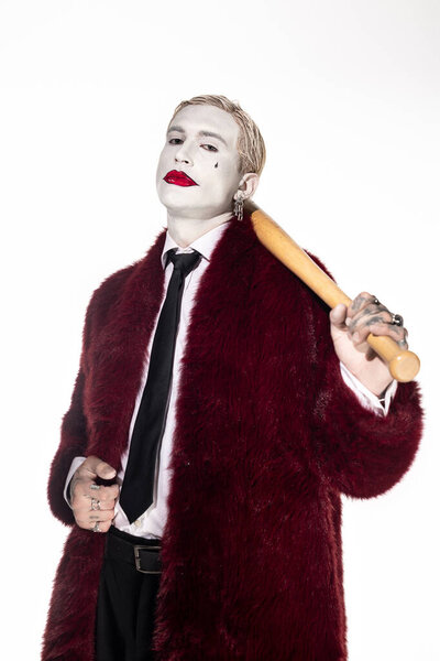 A handsome young man dressed in a vibrant Joker costume poses confidently, holding a bat.