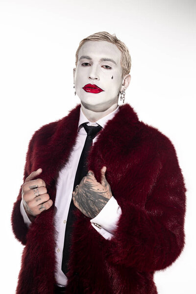 Красивый молодой человек носит впечатляющий костюм Джокера с ярким макияжем для Хэллоуина весело.