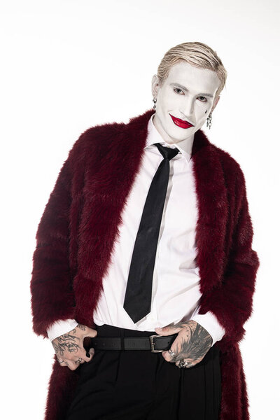 Красивый молодой человек демонстрирует свой творческий костюм Джокера с ярким макияжем и стильной одеждой.