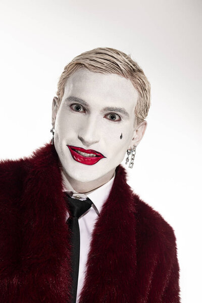 Молодой человек показывает впечатляющий костюм Джокера с драматическим макияжем на Хэллоуин.